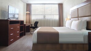 Una habitación de hotel con cama, escritorio, silla, televisor y cortinas.