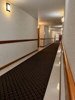 Un pasillo de hotel con alfombra estampada, paredes blancas y molduras de madera.