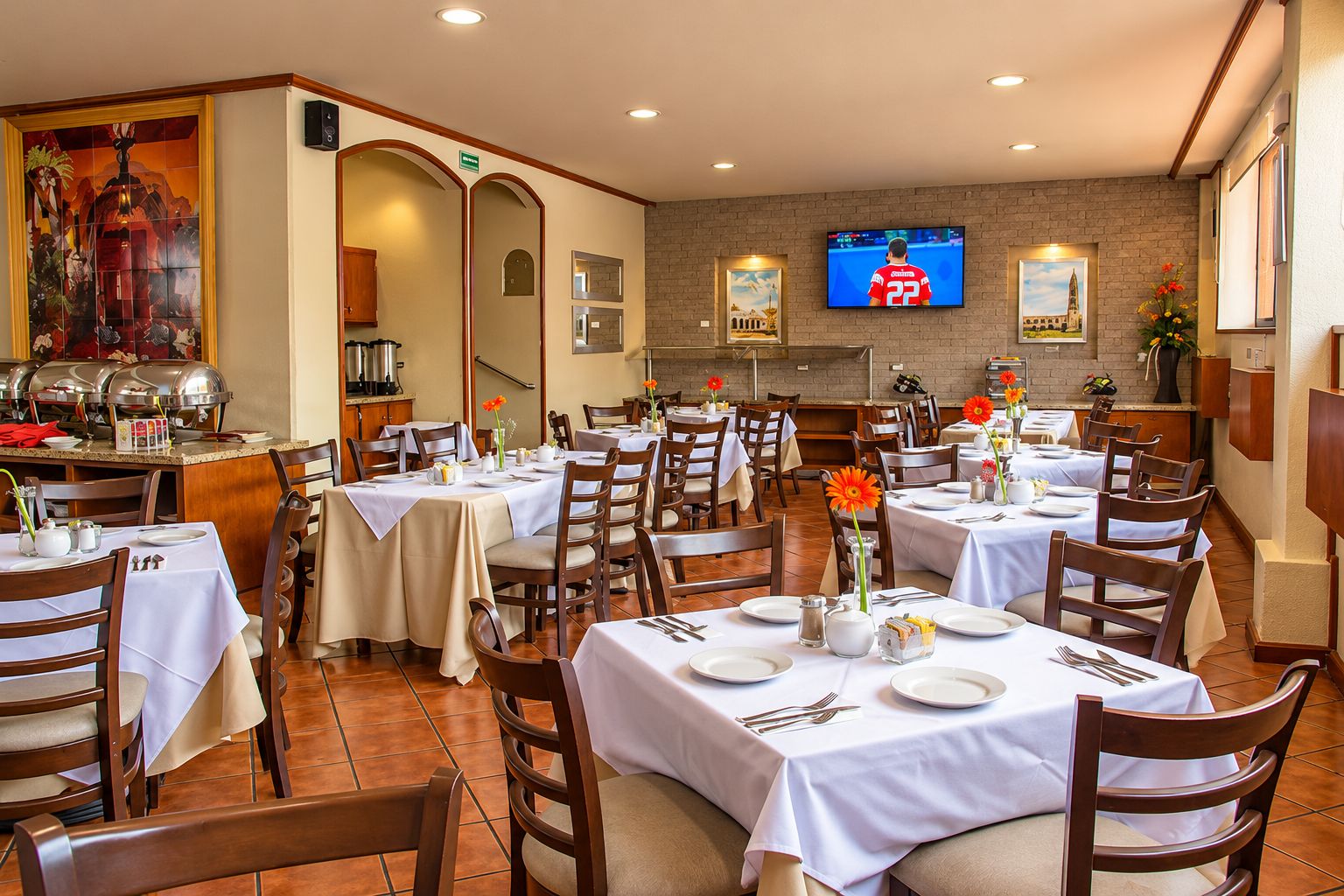 A dining area with multiple tables set for guests, a buffet station, and a television mounted on the wall.