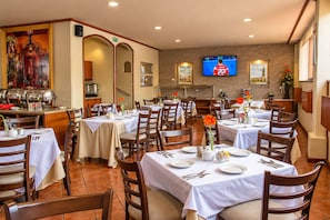 A dining area with multiple tables set for guests, a buffet station, and a television mounted on the wall.