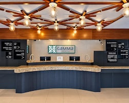 A hotel reception desk with a modern design, including a curved counter, a digital screen, and a ceiling with exposed beams and hanging light fixtures.
