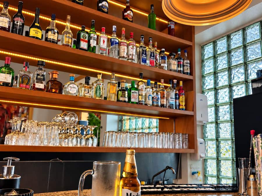 A bar area with shelves of liquor bottles, a copper pendant light, and a granite countertop with a bottle of Modena wine.