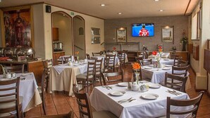 Un comedor con varias mesas dispuestas para los invitados, un televisor en la pared y una zona de buffet al fondo.