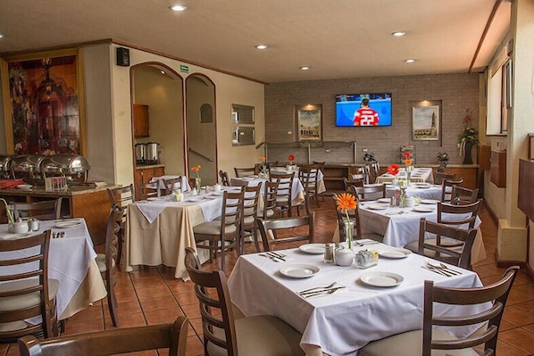 A dining area with multiple tables set for guests, a television mounted on the wall, and a buffet area in the background. - Gamma Durango Plaza Vizcaya (Durango)