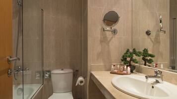 Un baño con ducha envuelta en vidrio, inodoro, lavamanos con espejo y artículos de aseo en la encimera.