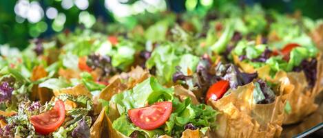 A tray of salad cups with various greens and a slice of tomato.