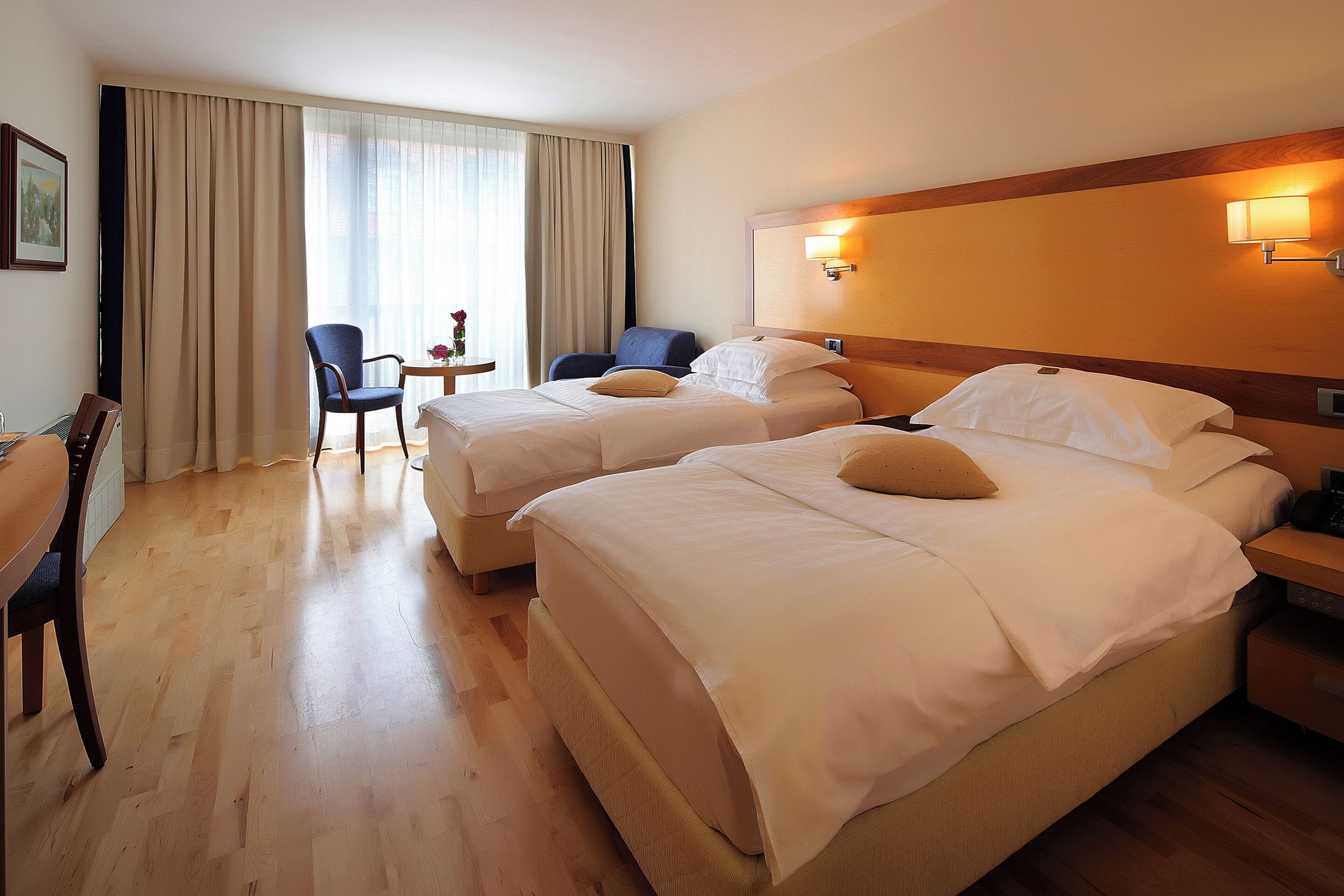 A hotel room with two beds, a desk, a chair, and a small table with a vase.