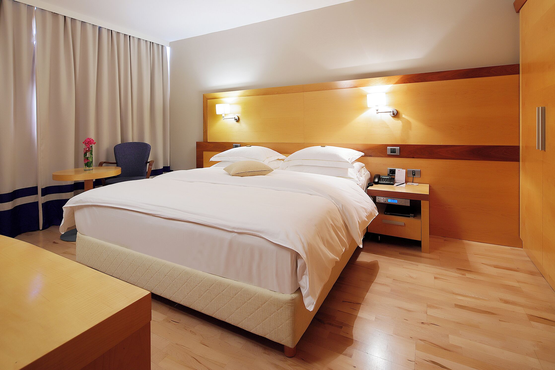 A hotel room with a large bed, bedside tables, a chair, and a desk.