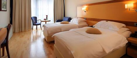 A hotel room with two beds, a desk, a chair, and a small table with a vase.