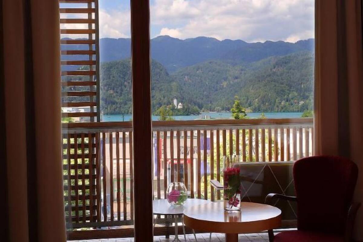 A balcony with a table and chair, a view of mountains and a lake, and a wooden fence.