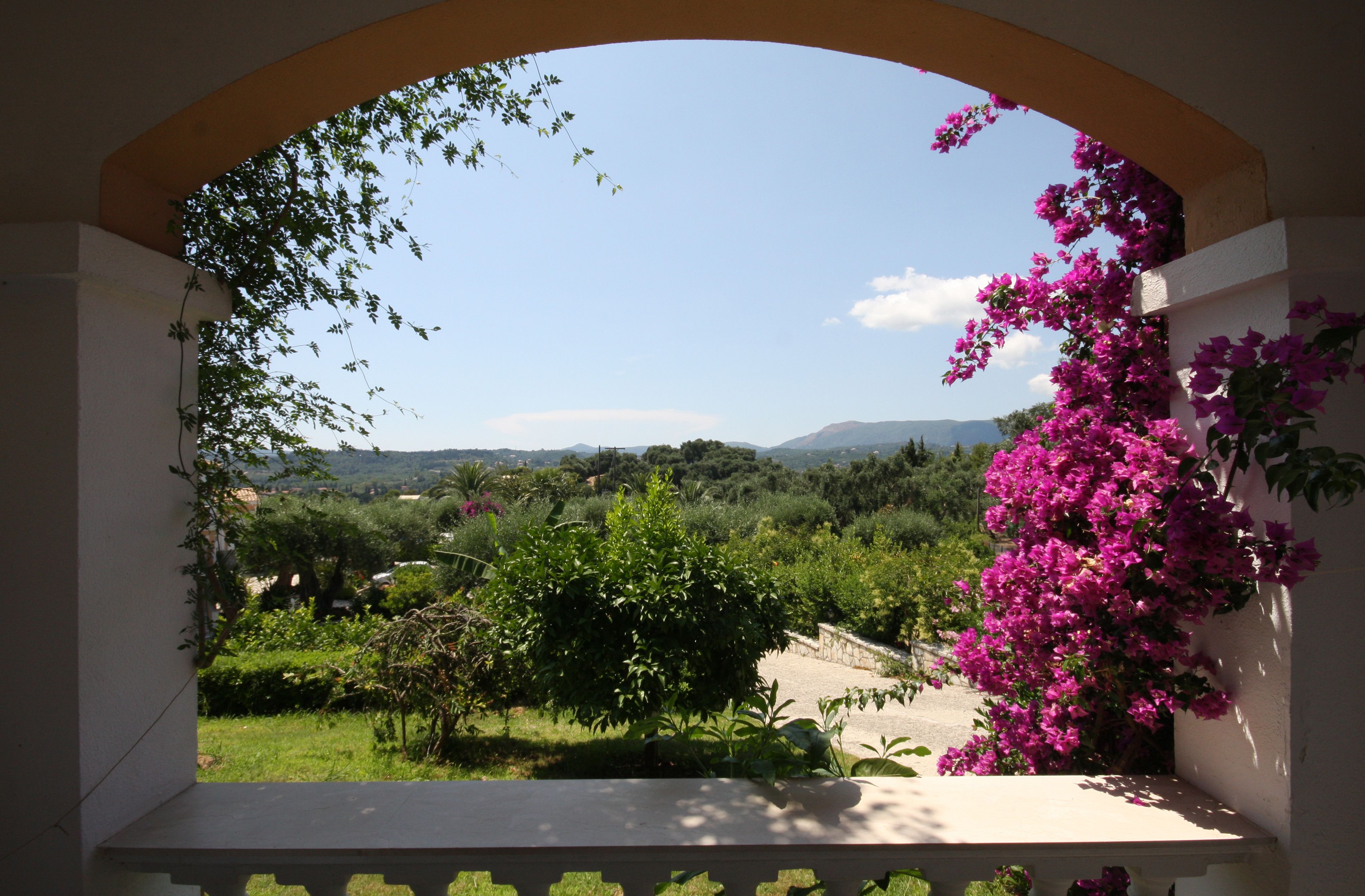 Un balcó amb vista a un jardí exuberant i muntanyes allunyades.