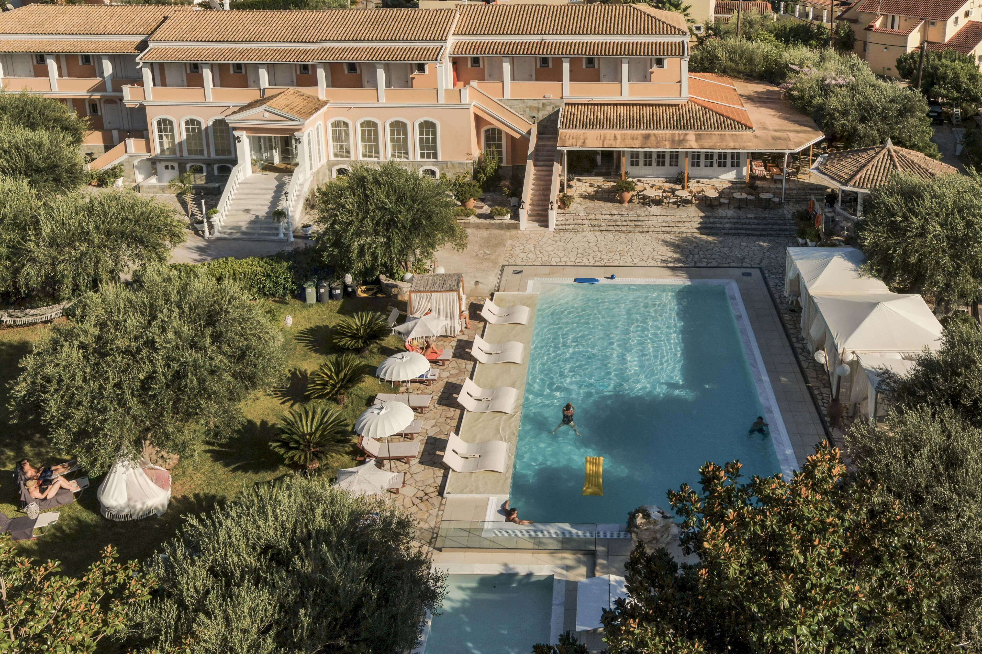 Vista aérea de um resort com piscina, espreguiçadeiras e um edifício grande com telhado de azulejos.