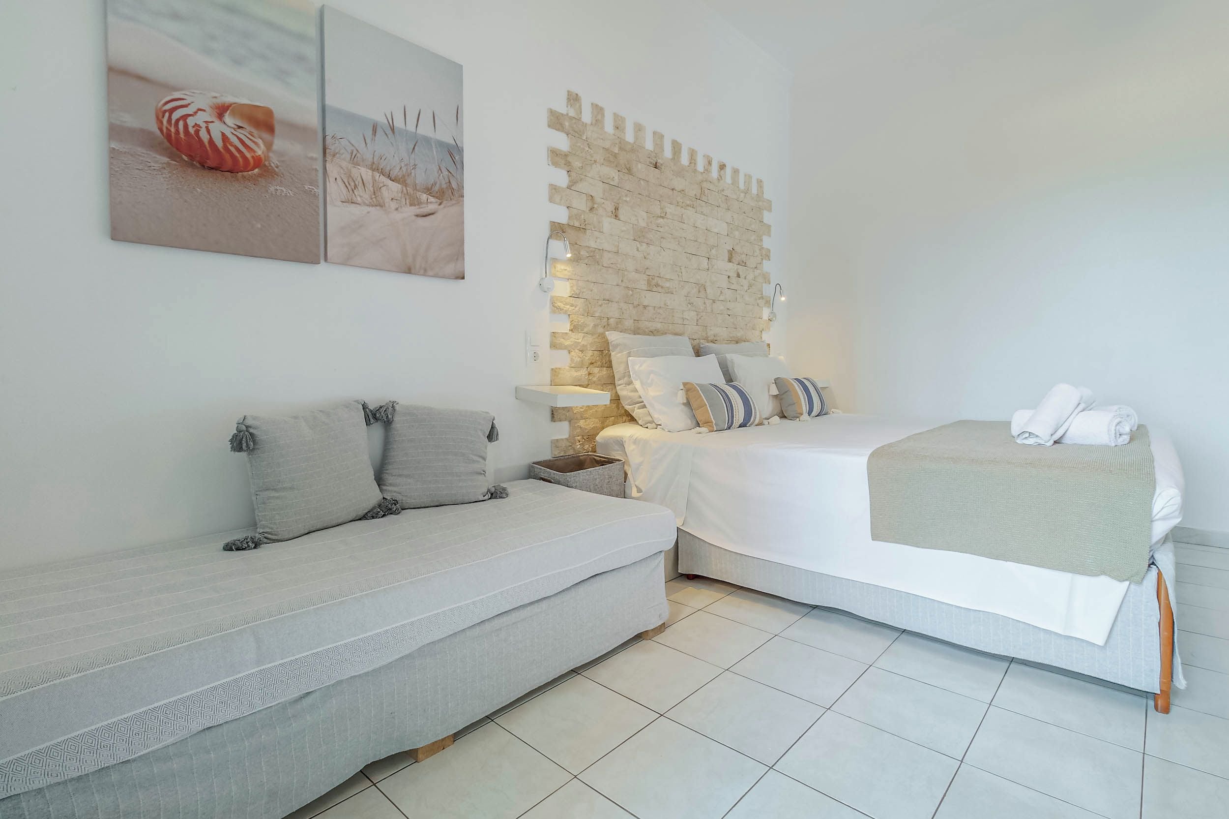 Un dormitorio con cama, sofá, mesita de noche y lámpara de pared.