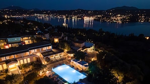 A resort with a swimming pool, multiple buildings, and a view of a lake at night. - Nefeli Hotel (Corfu)