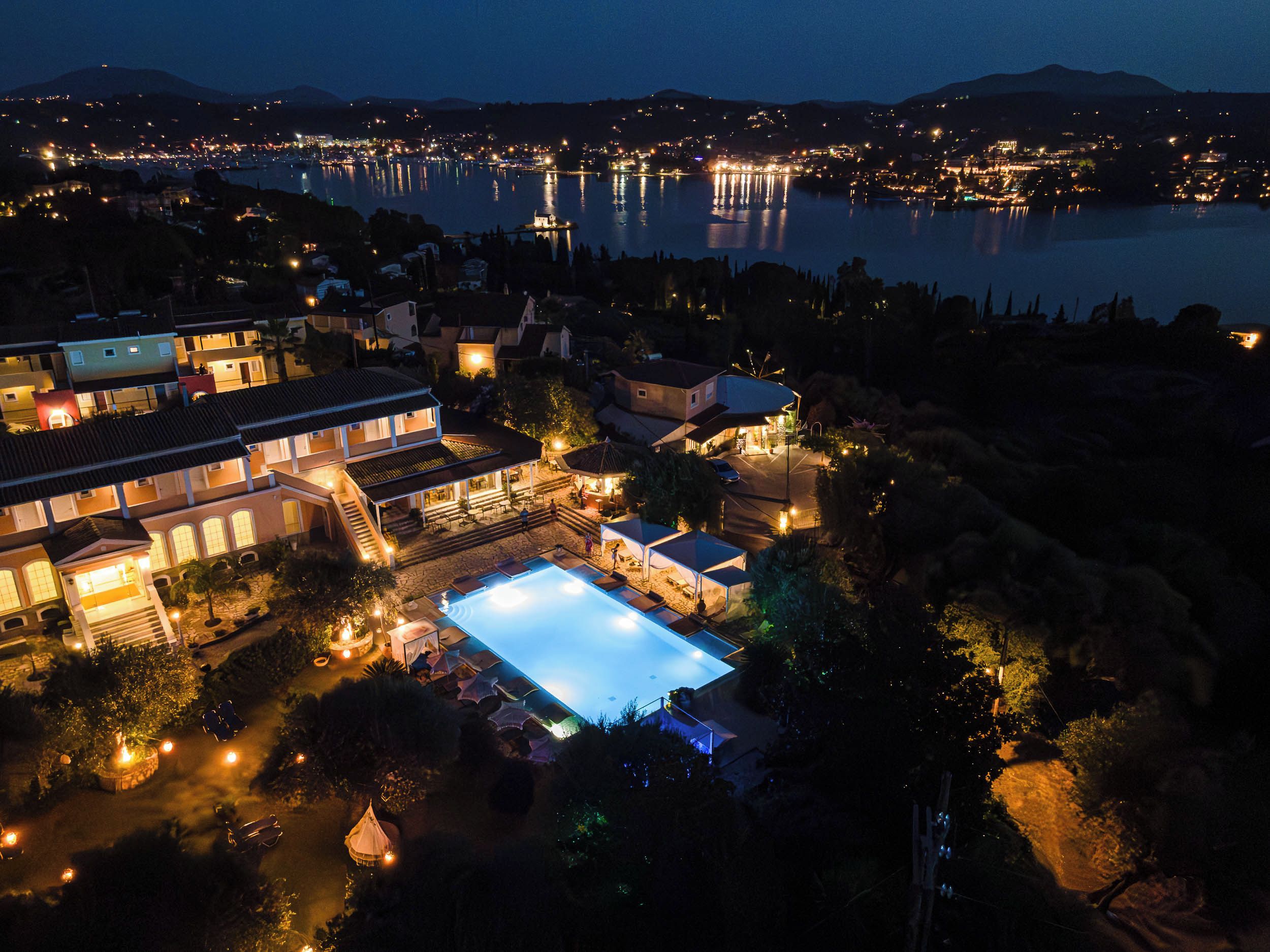 A residential area with a swimming pool, multiple houses, and a body of water in the background.