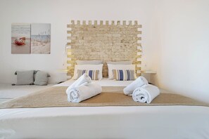 Une chambre d’hôtel avec une tête de lit ornée d’un motif en briques, un lit avec du linge de maison blanc, deux serviettes enroulées et un tapis tissé.