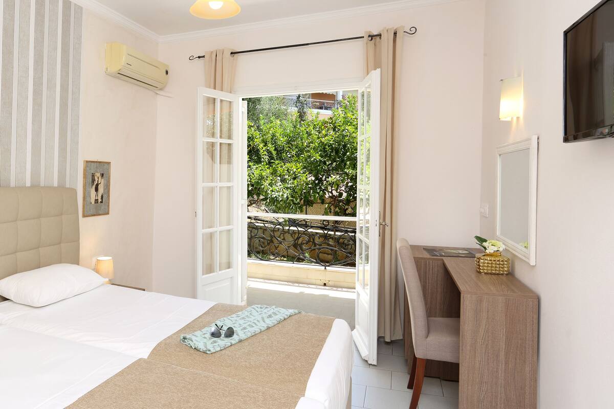 A bedroom with a bed, a bedside table, a mirror, and a view of the outdoors.