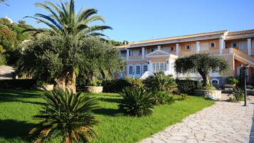 A well-maintained garden with palm trees and a stone pathway leading to a building with classical architecture.