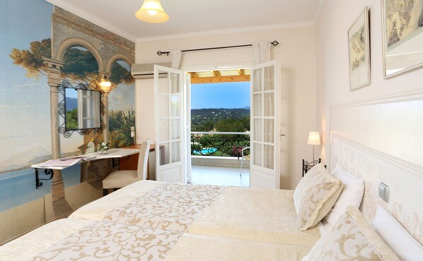 A bedroom with a bed, a desk, a chair, a mirror, and a view of a balcony with a pool.