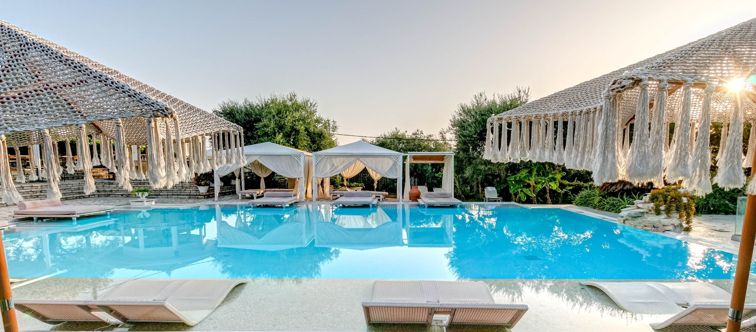 A pool area with lounge chairs, a white gazebo, and thatched umbrellas.