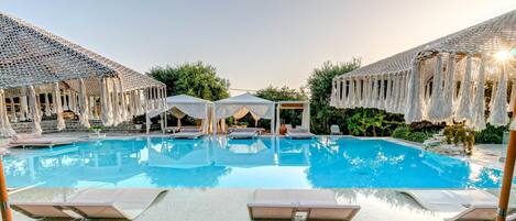 A pool area with lounge chairs, a white gazebo, and thatched umbrellas.