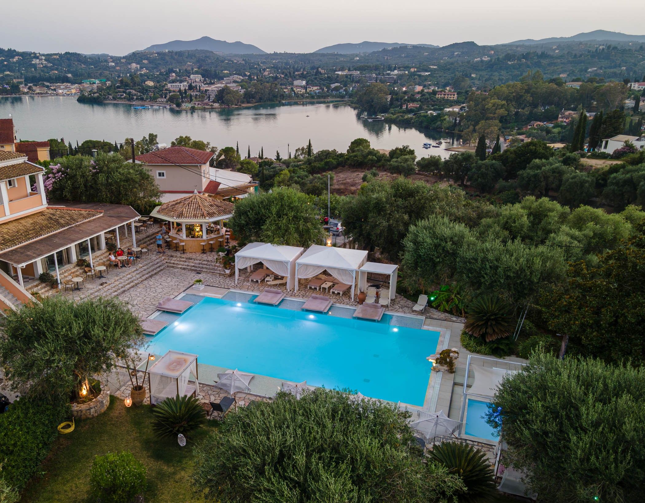 Un complexe hôtelier doté d’une piscine, d’un espace extérieur aménagé et offrant une vue sur un lac et des collines.