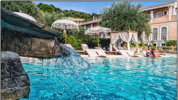 A pool with clear blue water, lounge chairs, and a rock feature. - Nefeli Hotel (Corfu)