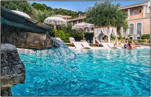 A pool with clear blue water, lounge chairs, and a rock feature.
