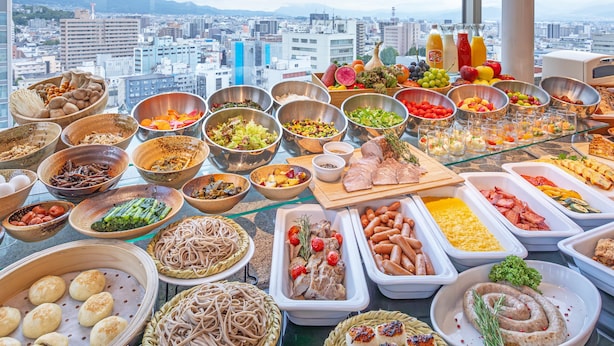 A buffet spread with various dishes and beverages, set against a cityscape view.