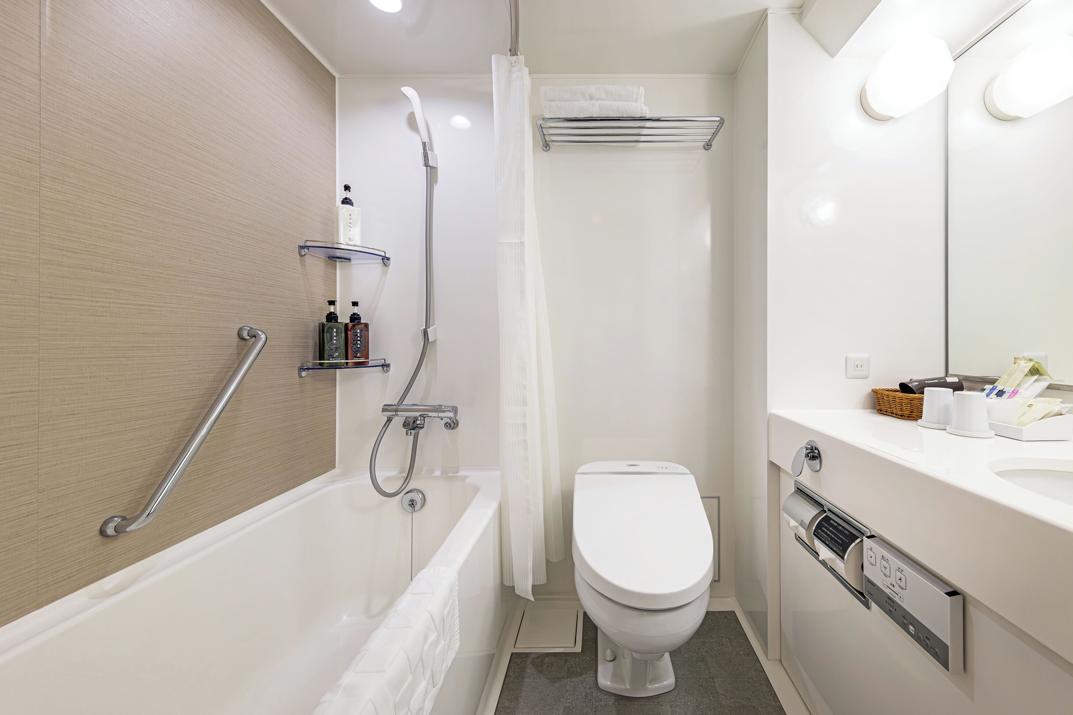 A modern bathroom with a bathtub, toilet, and shower. There are toiletries on a shelf and a towel rack.