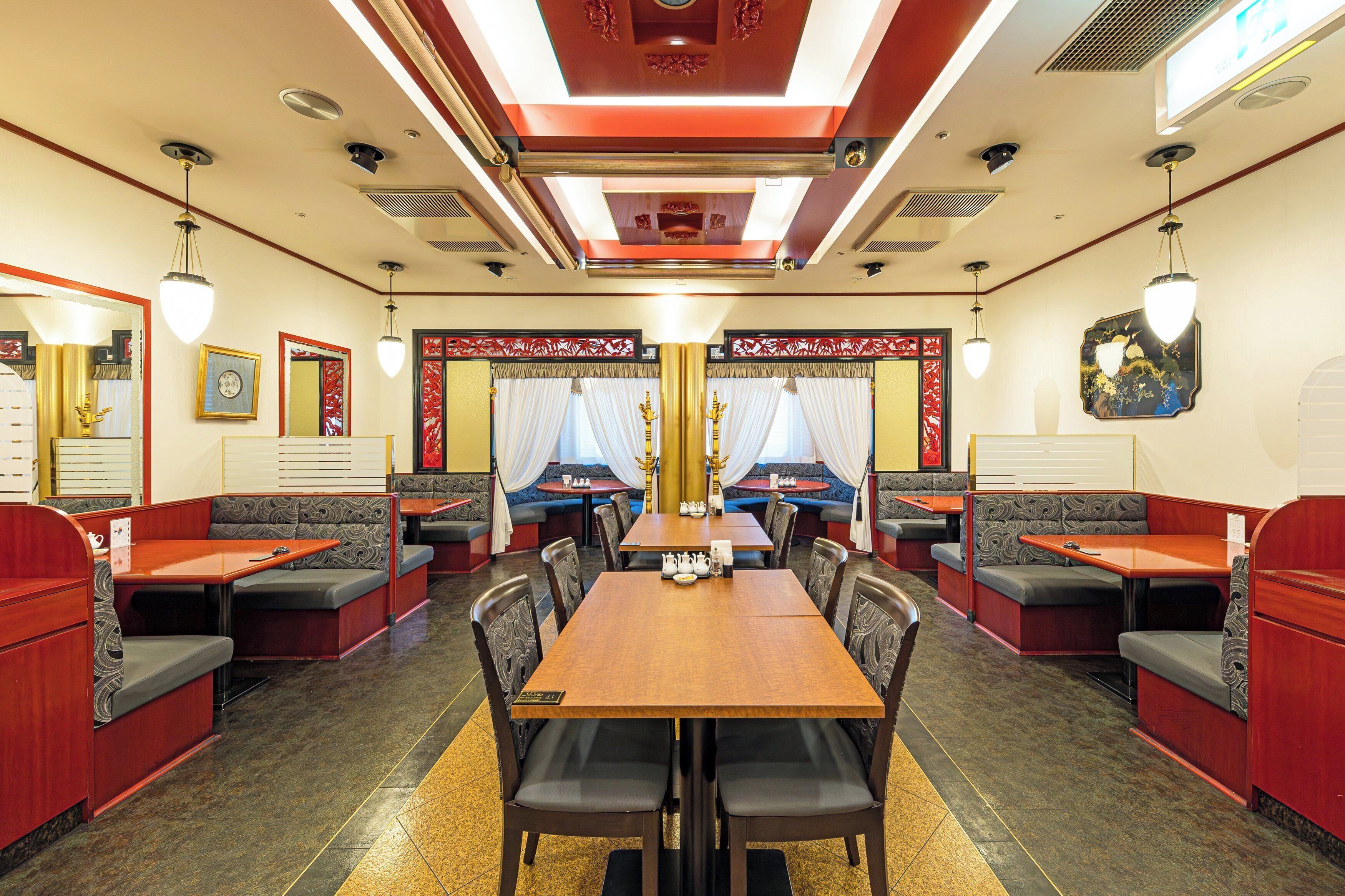 A restaurant with booths and tables, a central chandelier, and decorative wall panels.