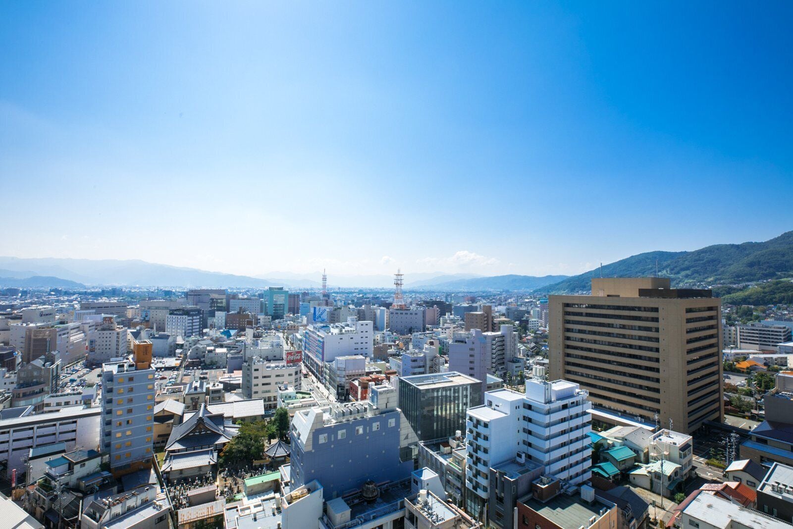 A cityscape with a mix of modern and traditional buildings, a clear sky, and distant mountains.