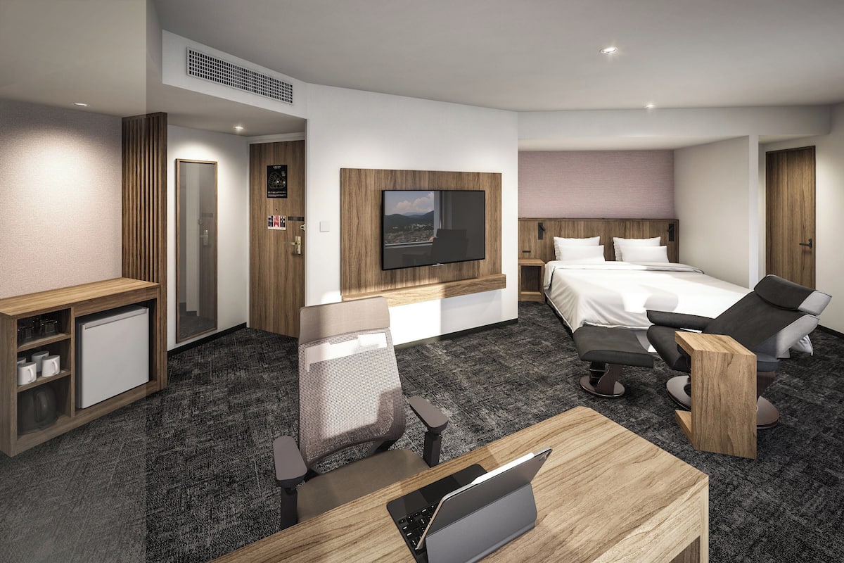 Et moderne hotelværelse med en seng, et skrivebord med en bærbar computer, en stol, et tv ophængt på væggen og et lille køleskab.