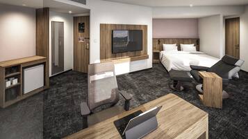 A modern hotel room with a bed, a desk with a laptop, a chair, a TV mounted on the wall, and a small refrigerator.