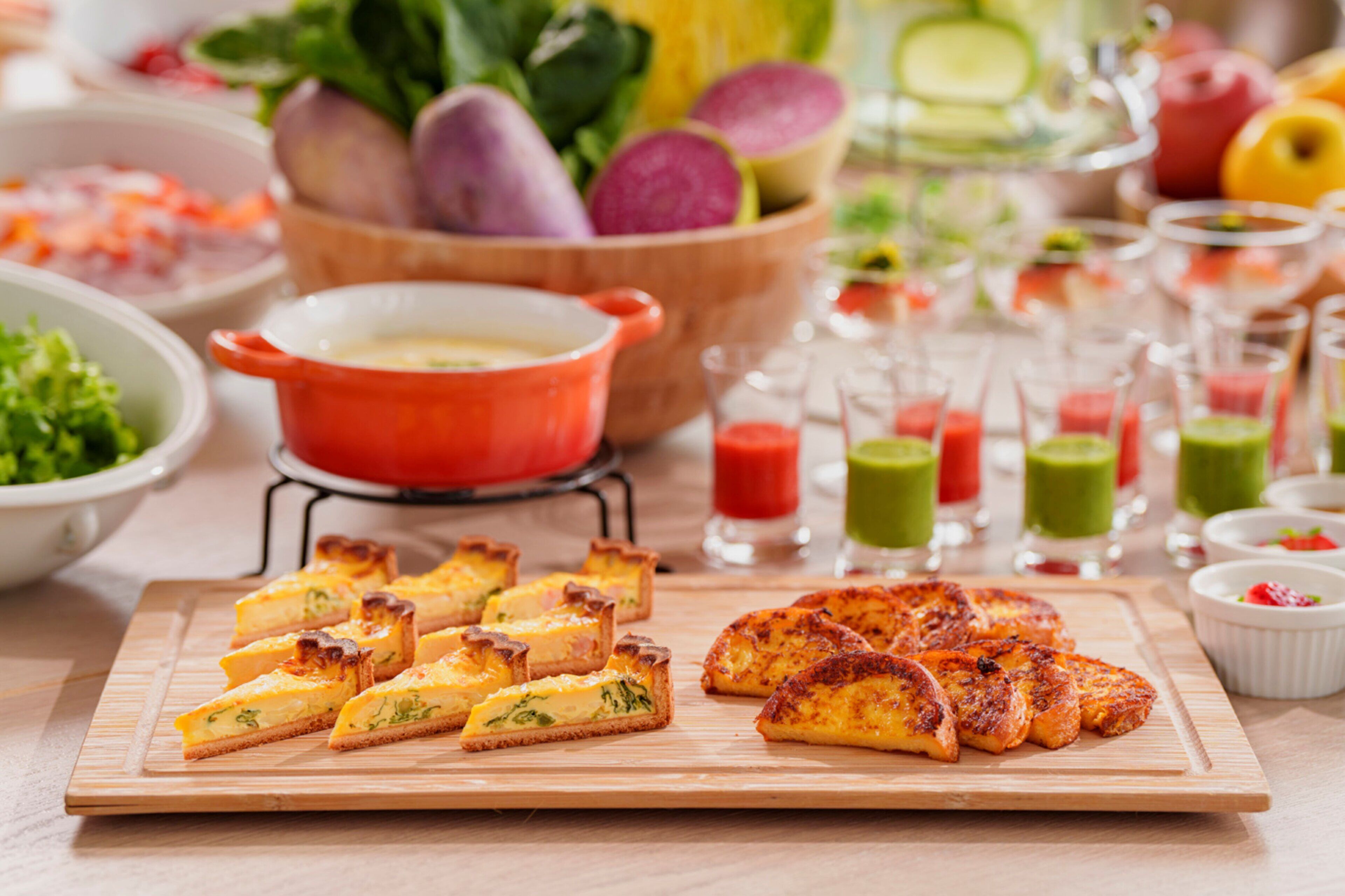 A variety of food items including quiches, a bowl of vegetables, and several glasses of beverages on a wooden table.