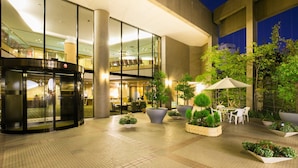 A hotel entrance with a revolving door, indoor seating area, and outdoor patio with tables and chairs.