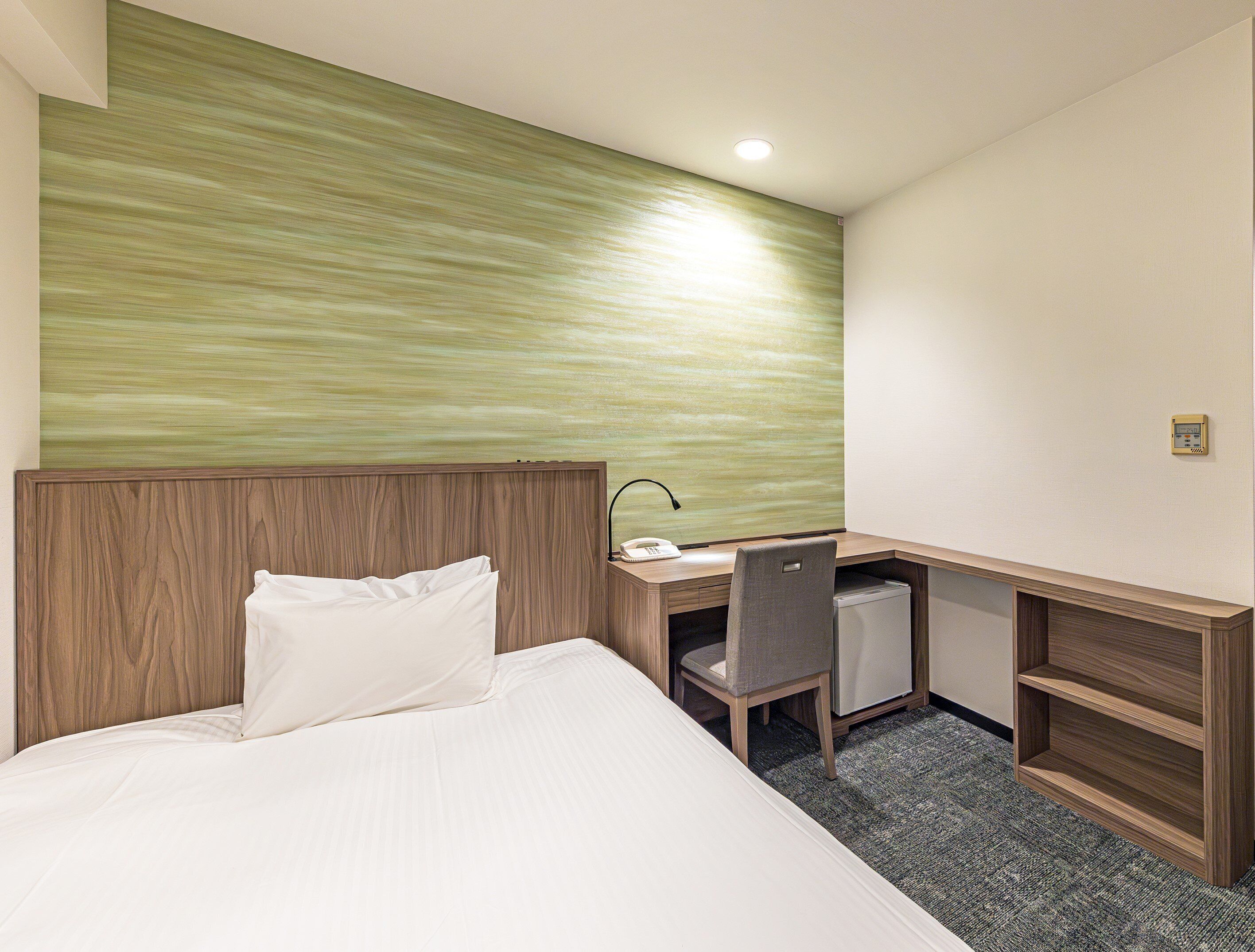A hotel room with a bed, a desk, a chair, and a small refrigerator.