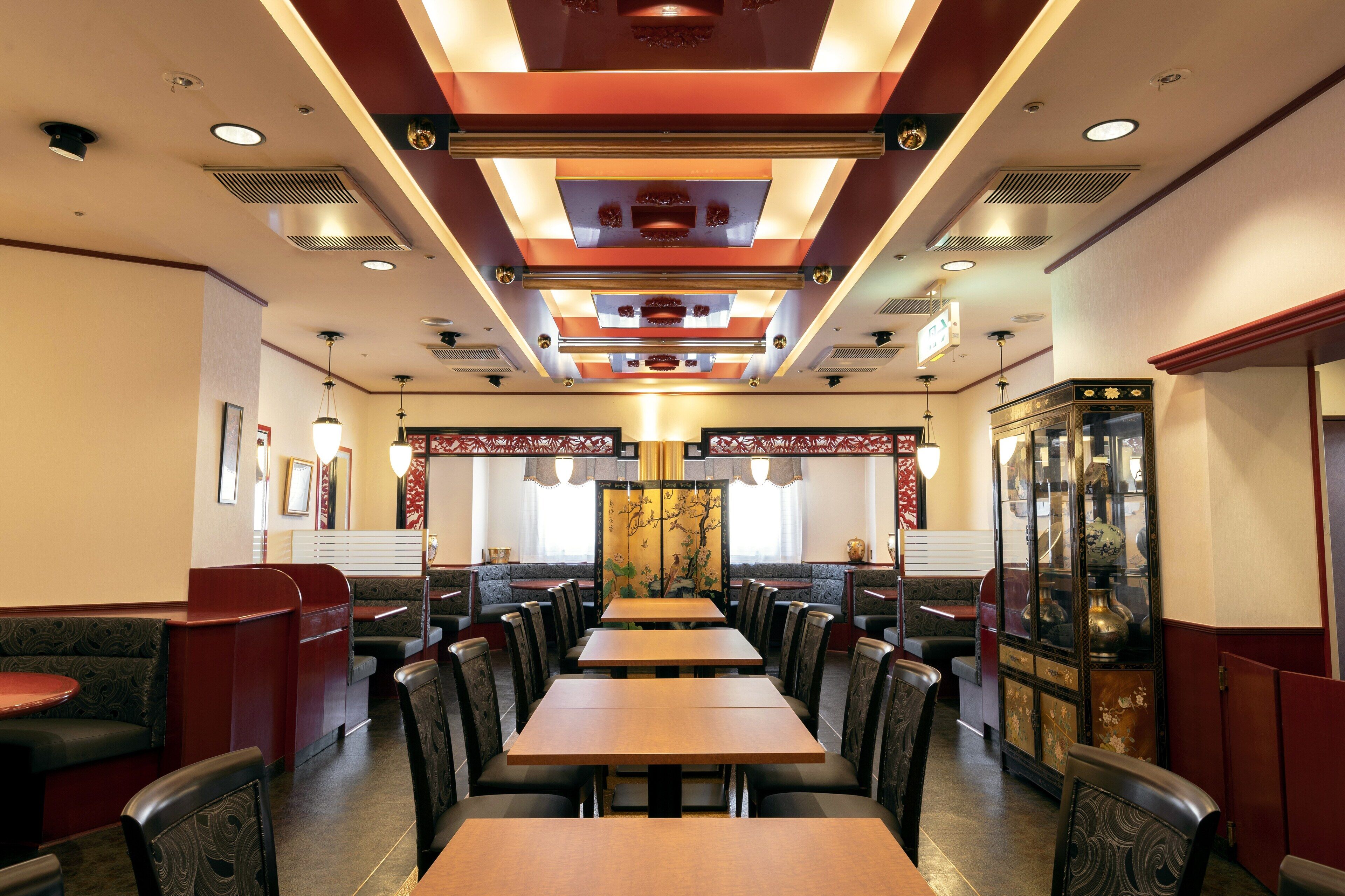 A restaurant with booths and tables, a decorative ceiling, and a traditional cabinet with glass doors.