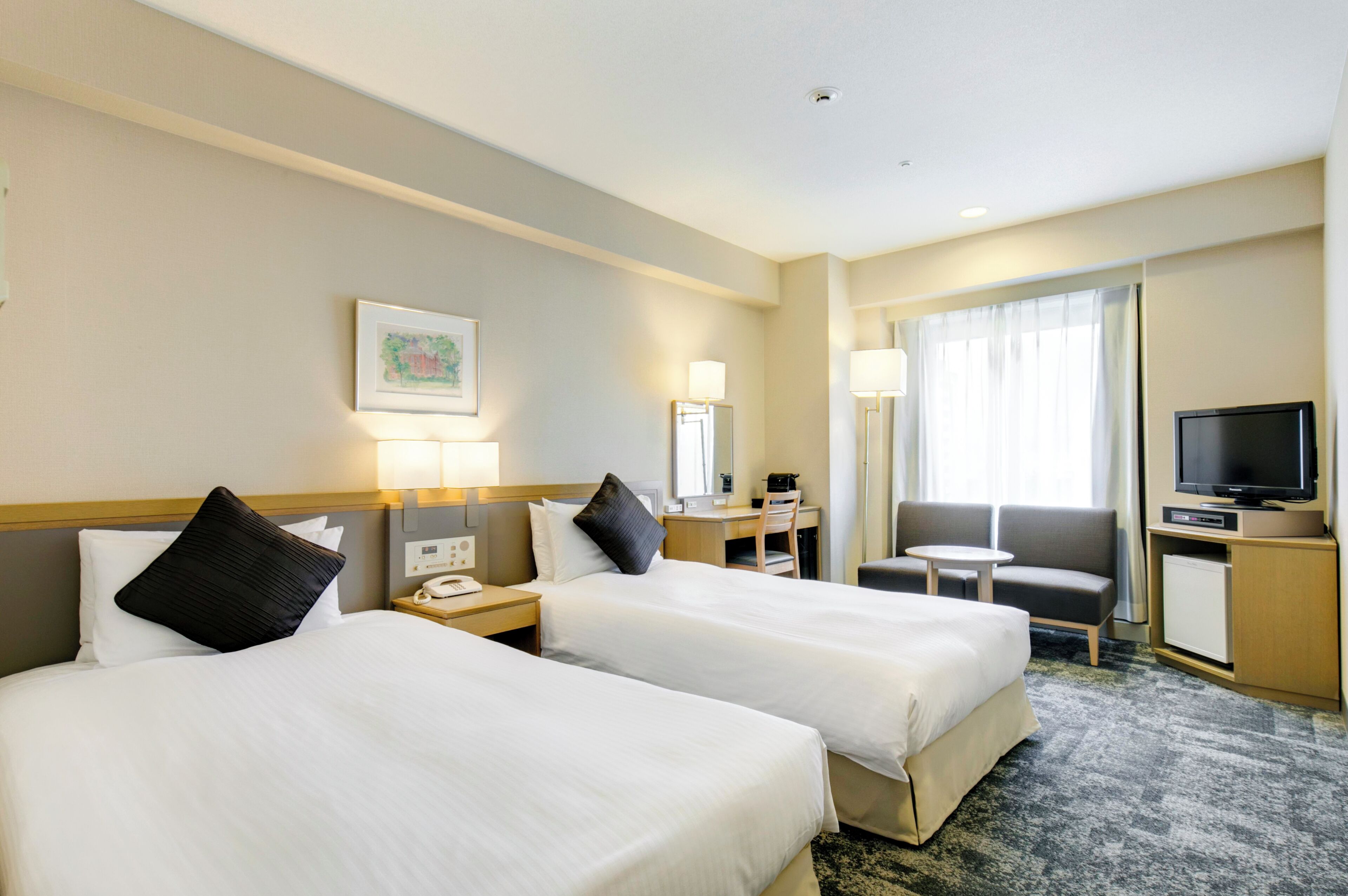 A hotel room with two beds, a desk, a chair, a television, and a window with curtains.