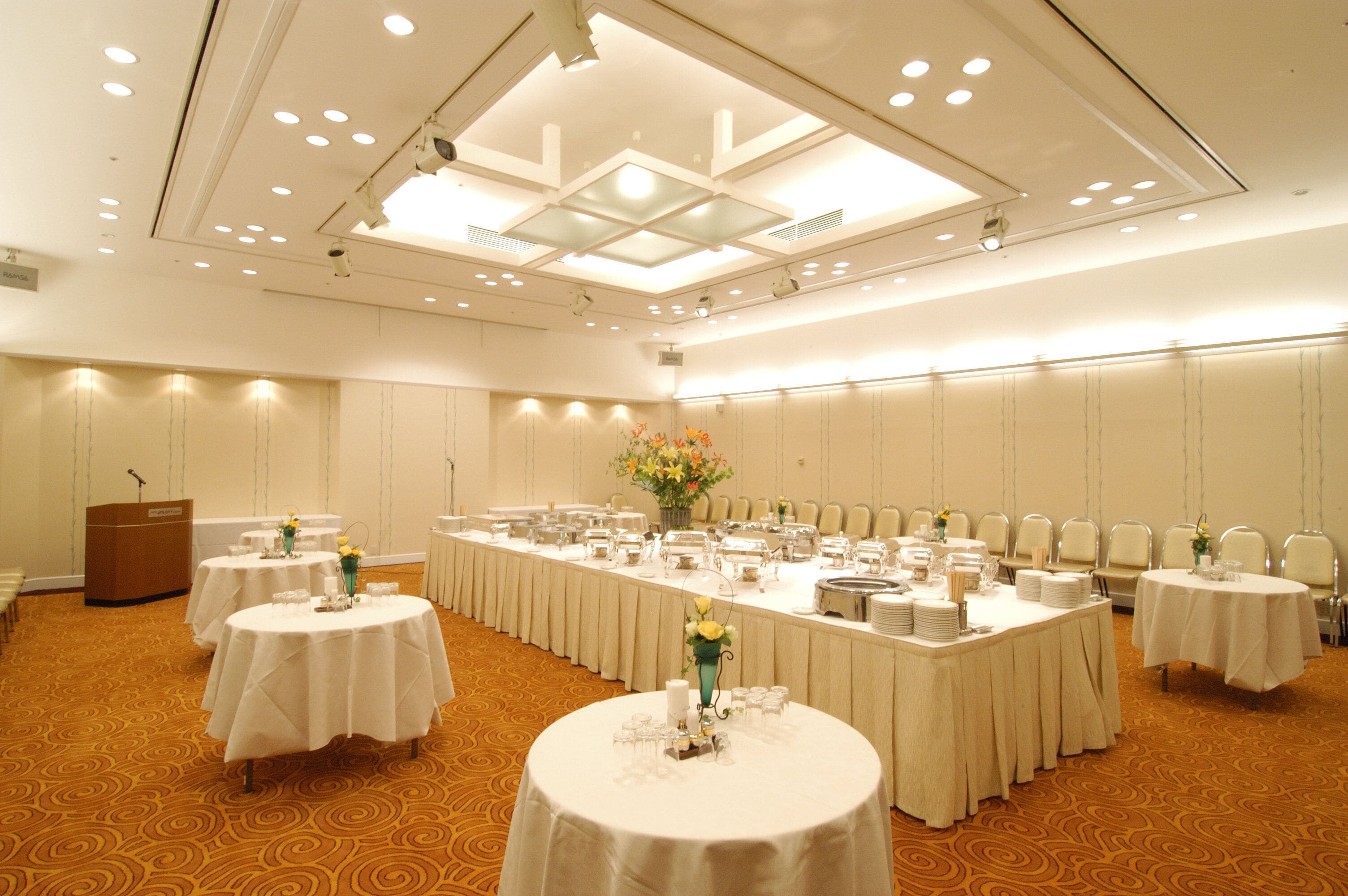 A conference room with multiple tables, a podium, and a ceiling with recessed lighting.
