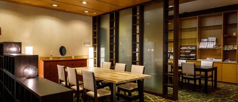 A conference room with a wooden table and chairs, a bookshelf, and a patterned carpet.