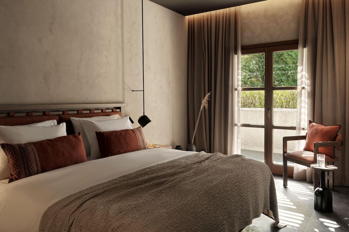 Un dormitorio con una cama grande, una mesita de noche, una silla y una ventana con cortinas.