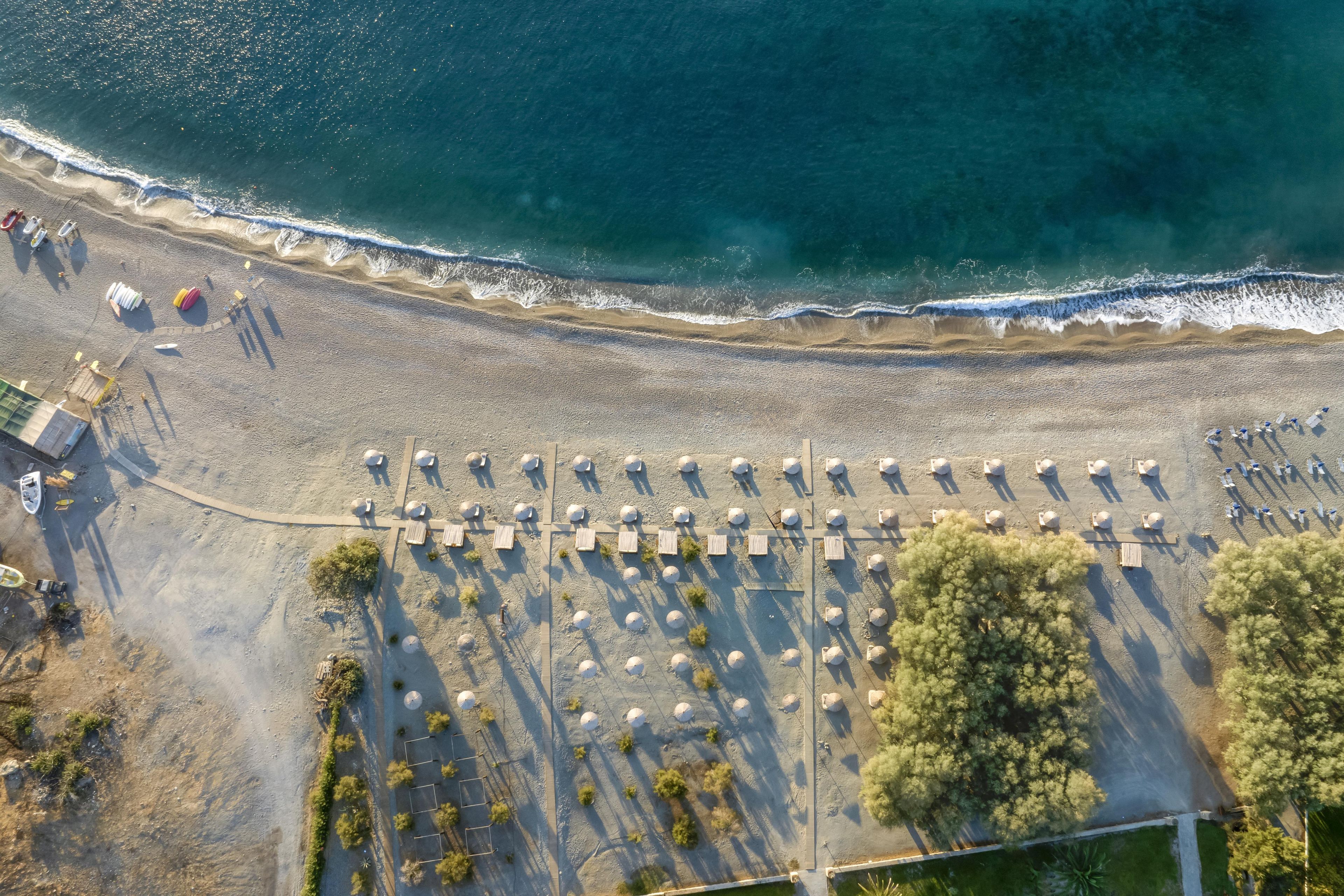 An aerial view of a beach with rows of umbrellas and sun loungers, a sandy beach, and a clear view of the ocean.