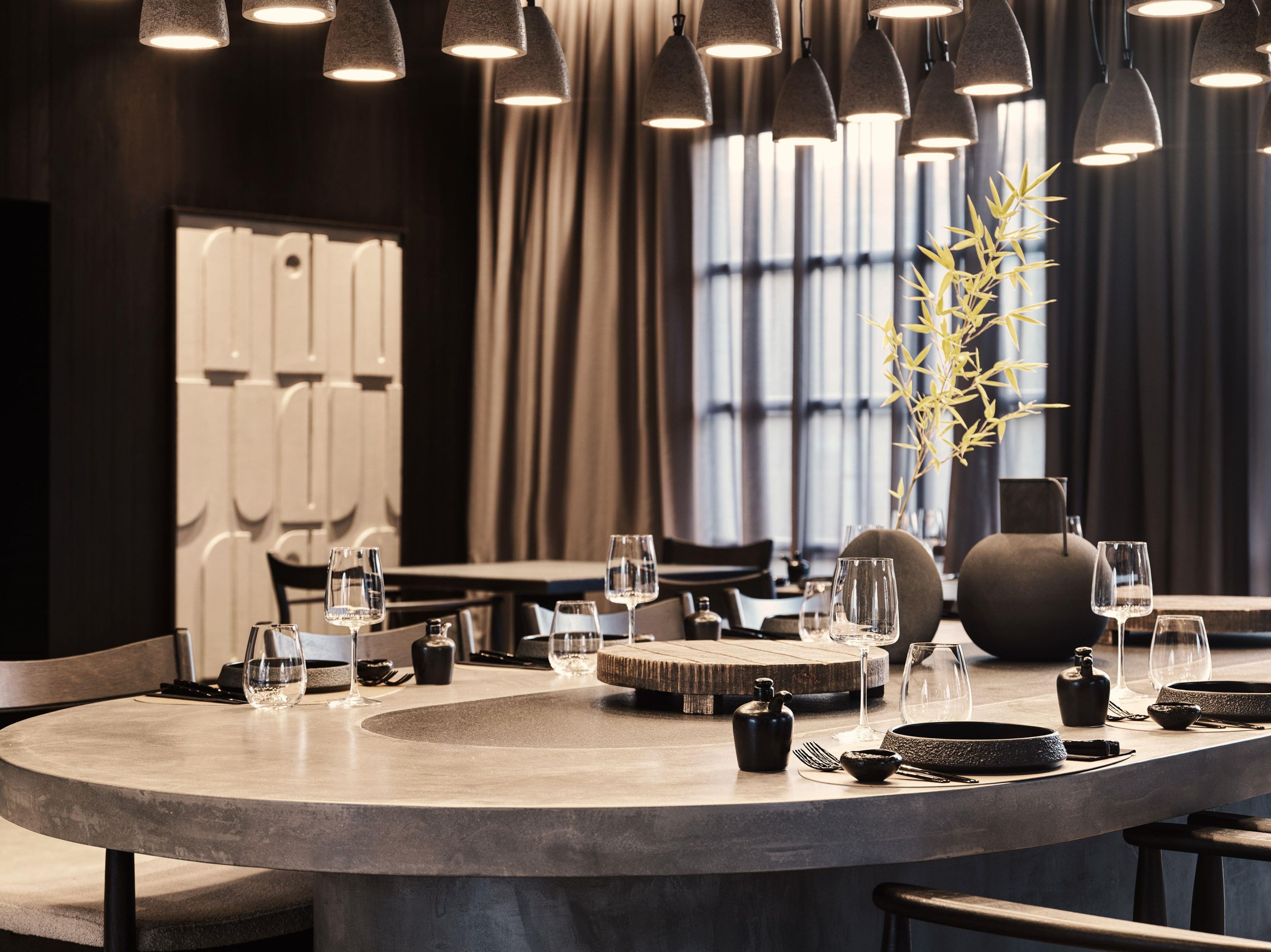 Un espace de restauration moderne avec une table ronde, plusieurs chaises et un éclairage suspendu au plafond.