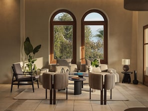 Amplia sala de estar con un conjunto de sofá, una mesa de centro y dos sillones. Hay ventanas grandes con arcos, una planta en maceta y una lámpara sobre una mesita.