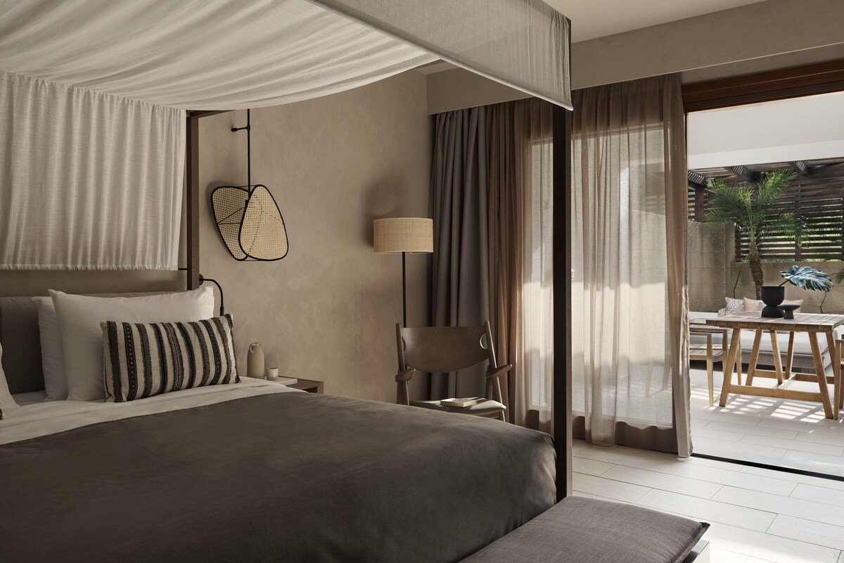 Une chambre d’hôtel moderne, dotée d’un grand lit, d’un bureau, d’une chaise et offrant une vue sur la terrasse extérieure.