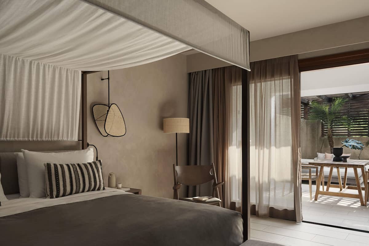 Una habitación de hotel moderna con una cama grande, un escritorio, una silla y vistas al patio exterior.