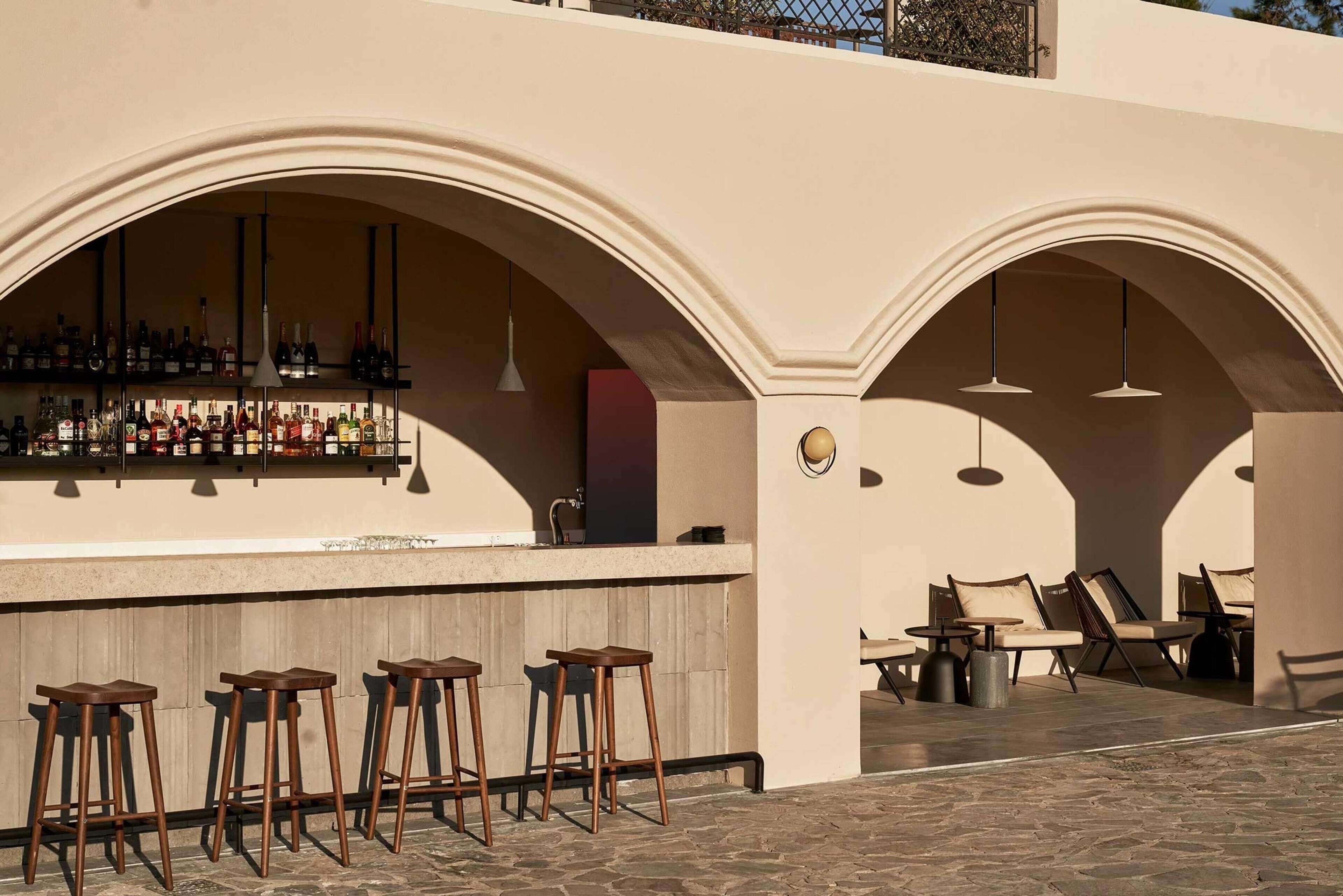An outdoor bar area with a counter, stools, and seating under arches.