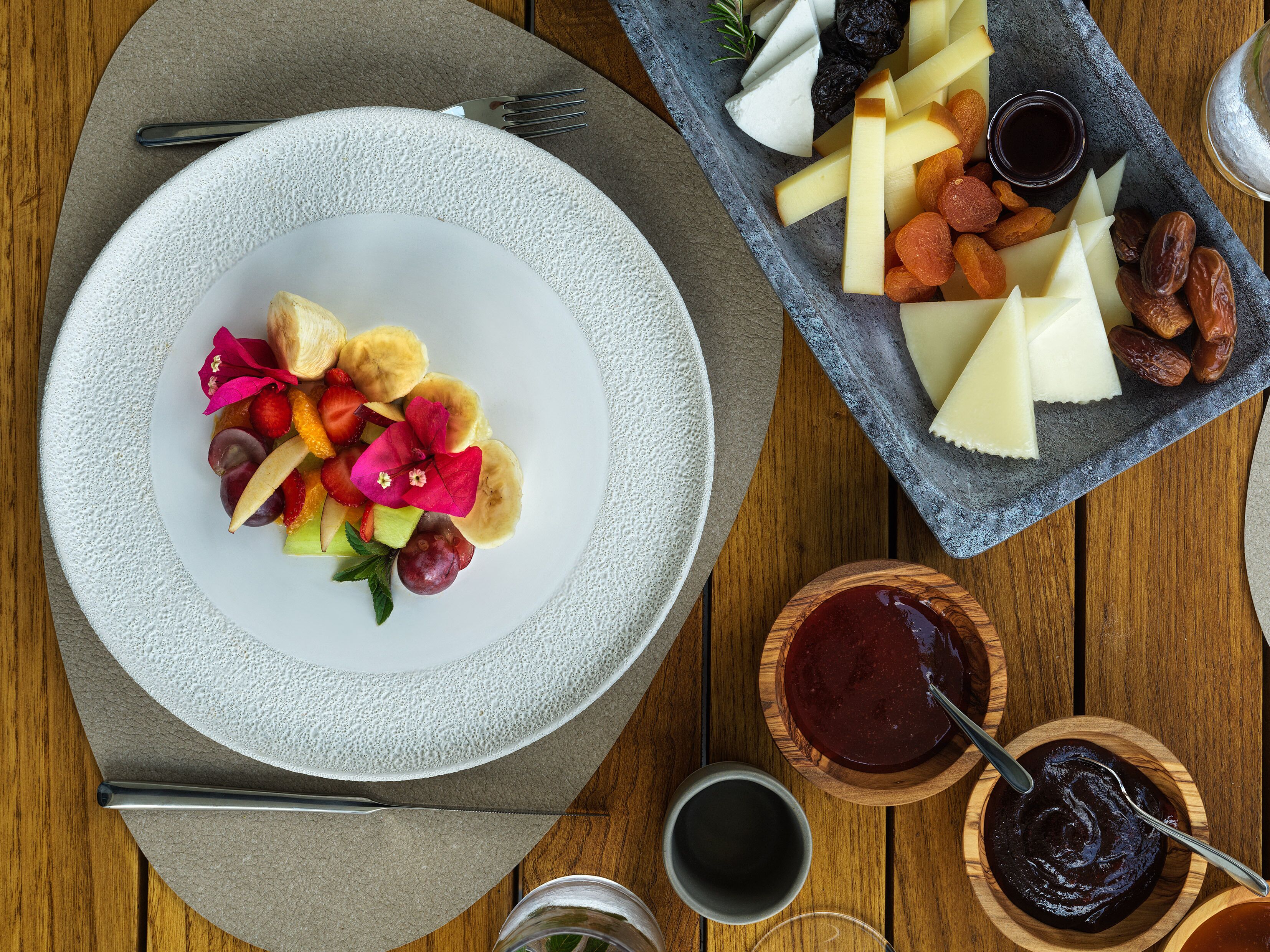 A table with a plate of fruit and cheese, a bowl of jam, and a glass of water.