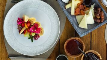 A table with a plate of fruit and cheese, a bowl of jam, and a glass of water.